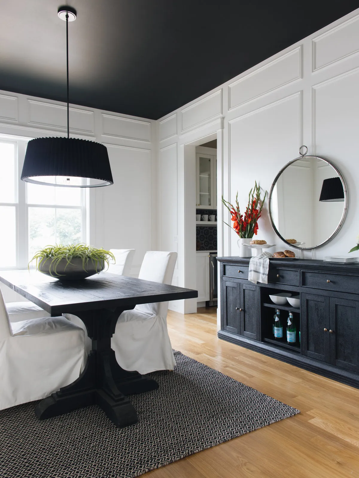 A dark ceiling sits above white paneling, pale chairs and a black pedestal table.