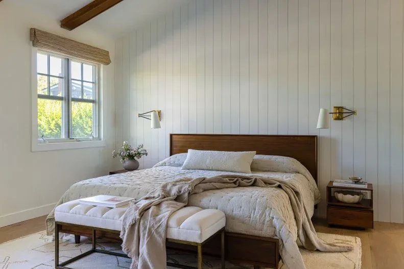 White vertical bedroom boards frame a simple timber bed and bedside storage beneath a sloping ceiling.