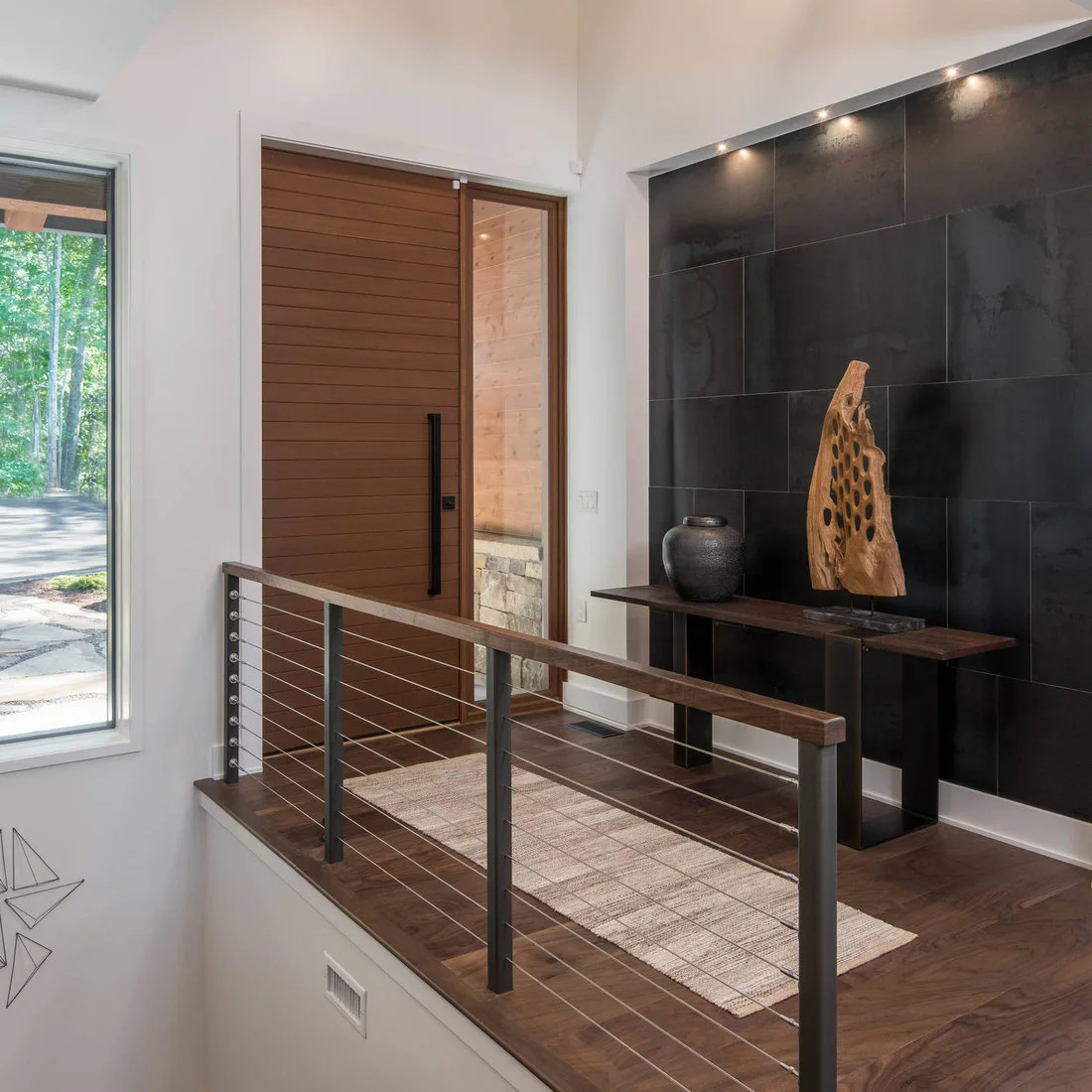 A narrow wood console against large dark wall panels beside a timber front door and stair railing