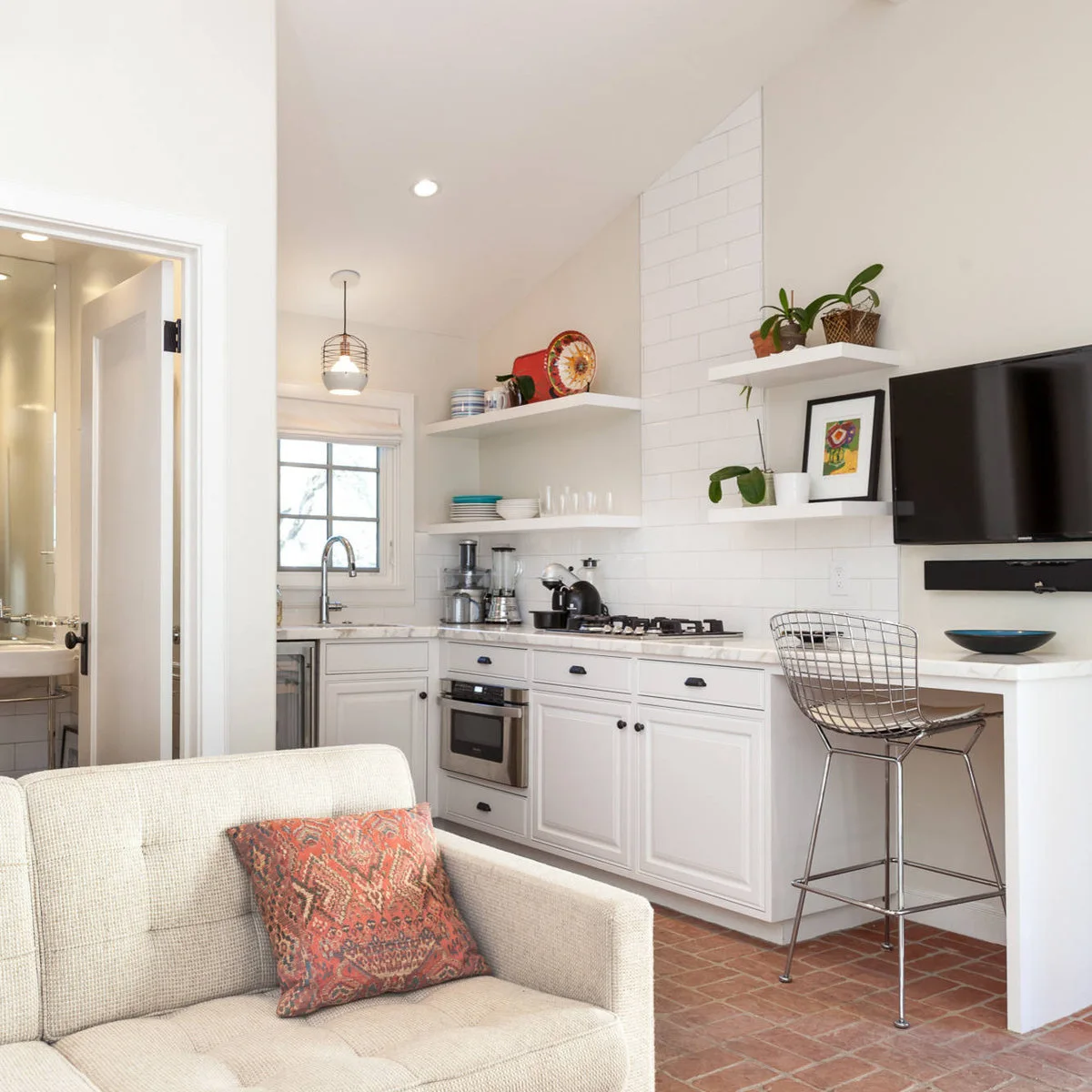 White kitchenette with a small cooktop, sink, open shelves and a single counter-height chair