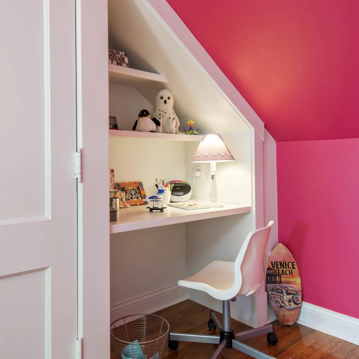 Small white desk and shelves beneath a sloping ceiling beside a bright pink wall