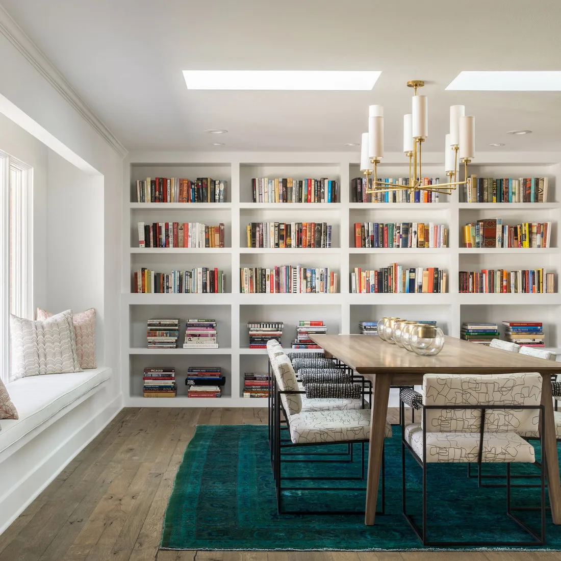 Deep teal rug beneath a wood dining table and patterned chairs in front of full-wall bookshelves