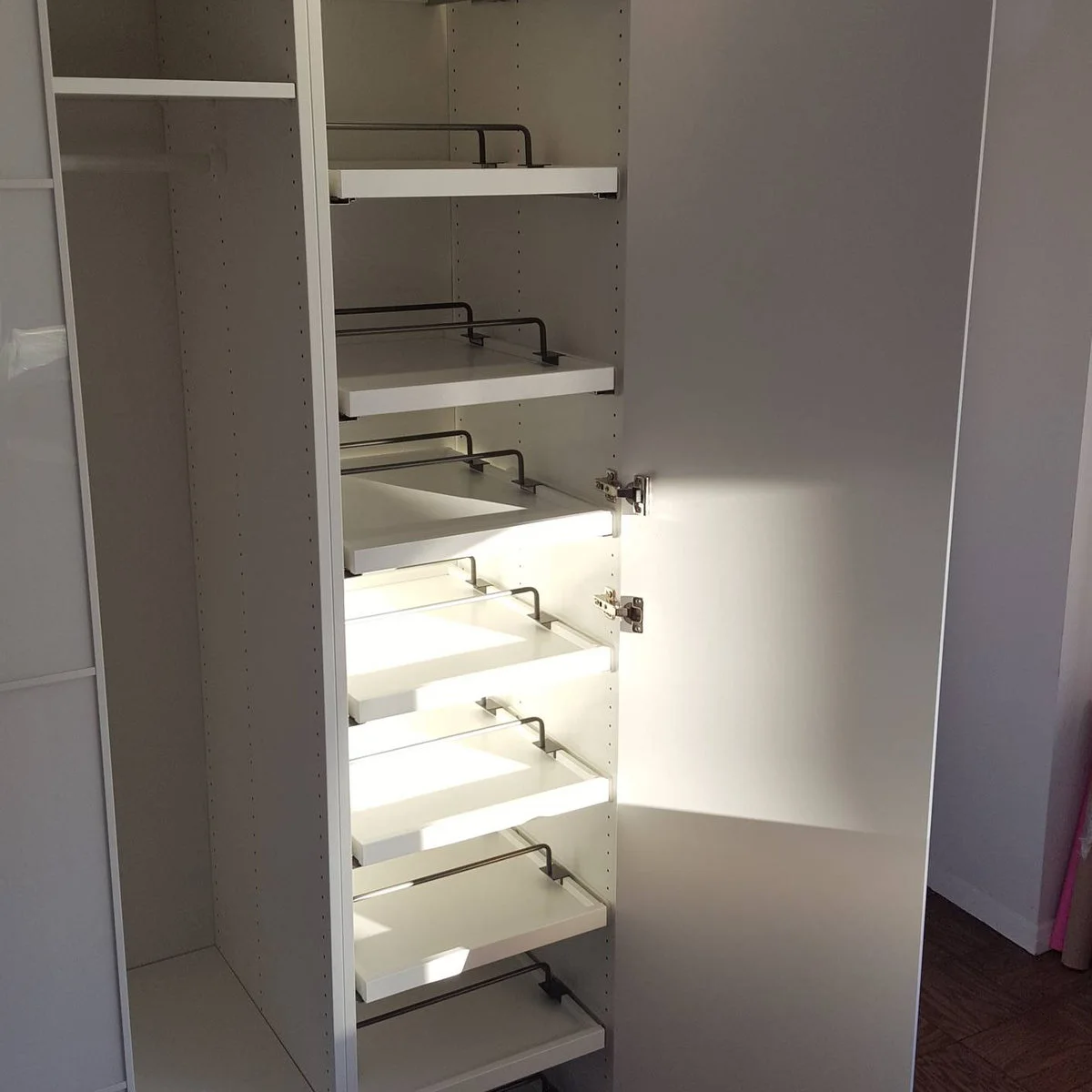 Narrow white PAX section with several shallow pullout shoe shelves behind an open door