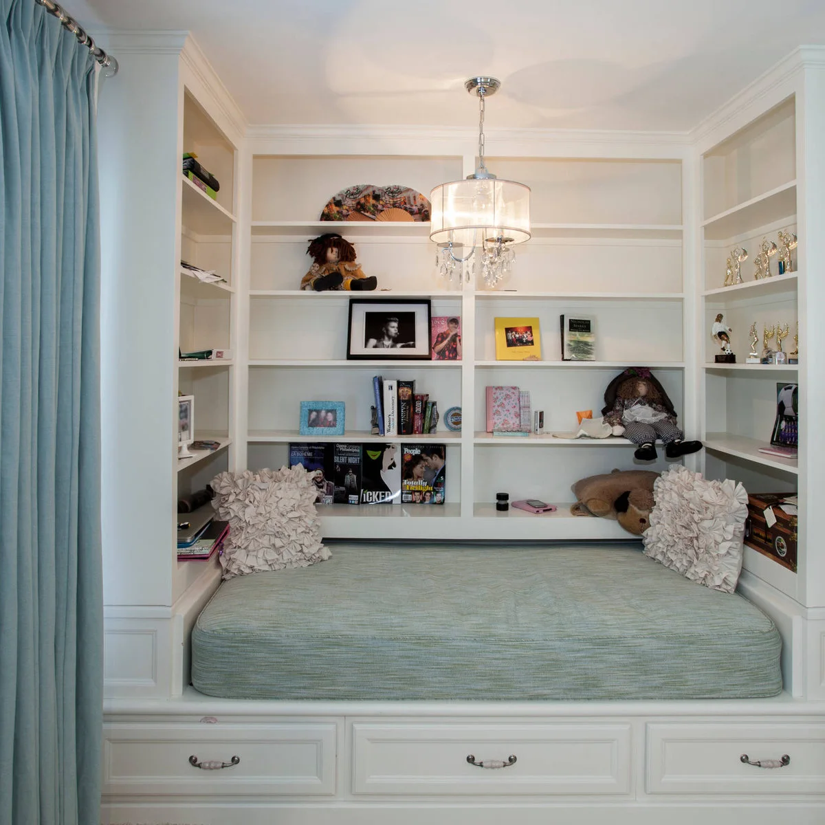 Built-in daybed with pale blue cushion, surrounding white shelves and drawers underneath