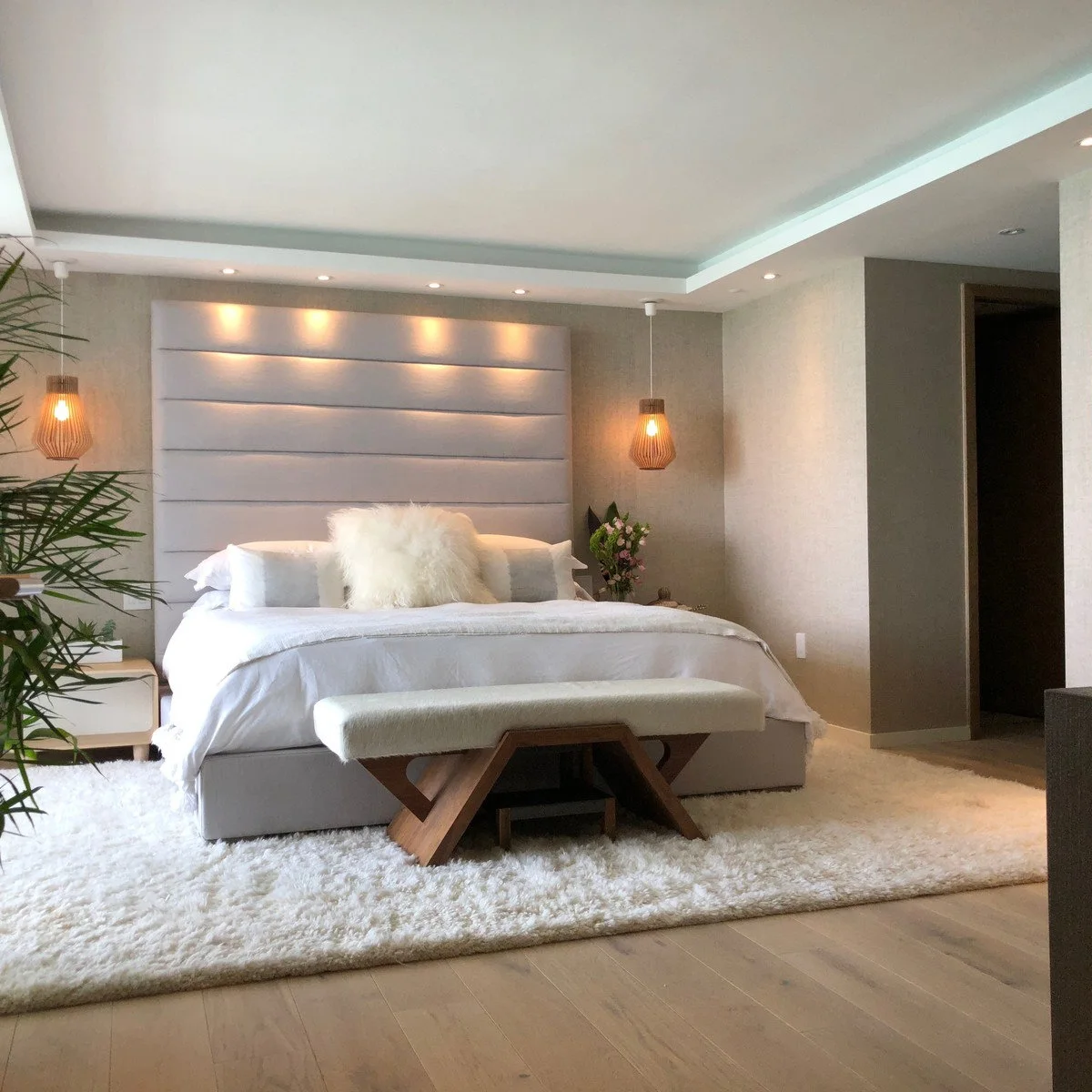 Pale bedroom with a tall padded headboard, small pendant lights and a bench