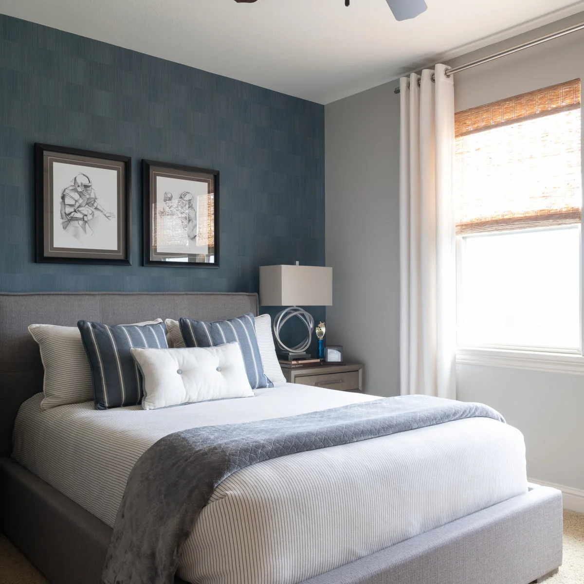 Compact bedroom with a blue textured wall, grey upholstered bed and two framed football sketches
