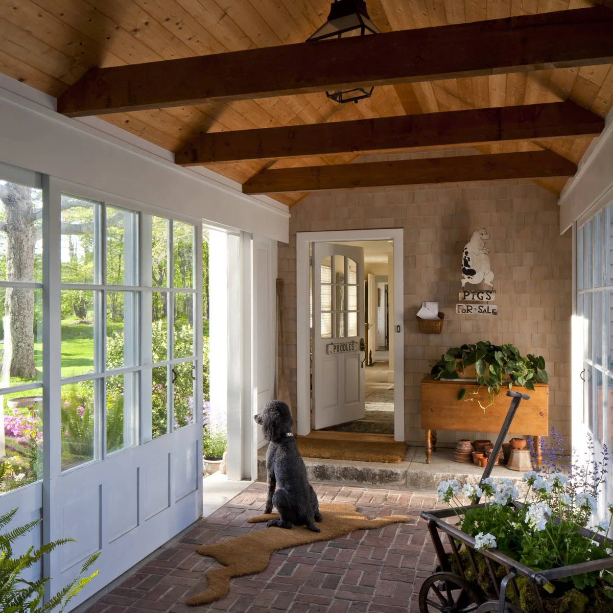 A brick-floored porch with pale blue glazed doors, a wooden drop-leaf table, flower pots and a dog by the doorway.
